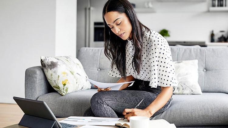 A young lady sits on her couch working on college loan paperwork.